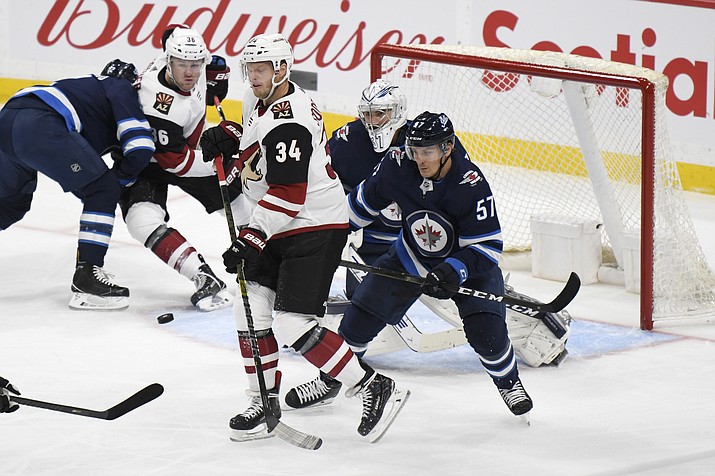 Winnipeg Jets’ Gabriel Bourque (57) and Arizona Coyotes’ Carl Soderberg (34) watch as the puck is shot toward Jets goalie Connor Hellebuyck during the first period of a game Tuesday, Oct. 15, 2019, in Winnipeg, Manitoba. (Fred Greenslade/The Canadian Press via AP)