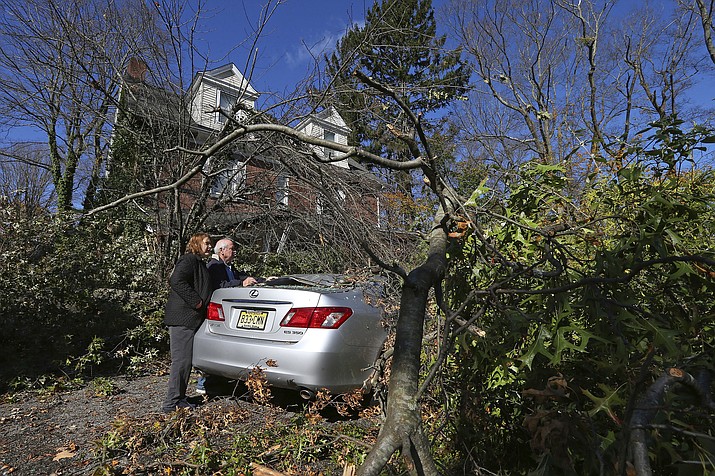 Lynda and Michael Behrens look at their crushed Lexus after an Oak tree from their backyard snapped and landed on both the car and front porch on Green Village Road, Friday, Nov. 1, 2019, in Madison, N.J. The borough was hit by high winds on heavy rain late the night before. (AP Photo/Rich Schultz)