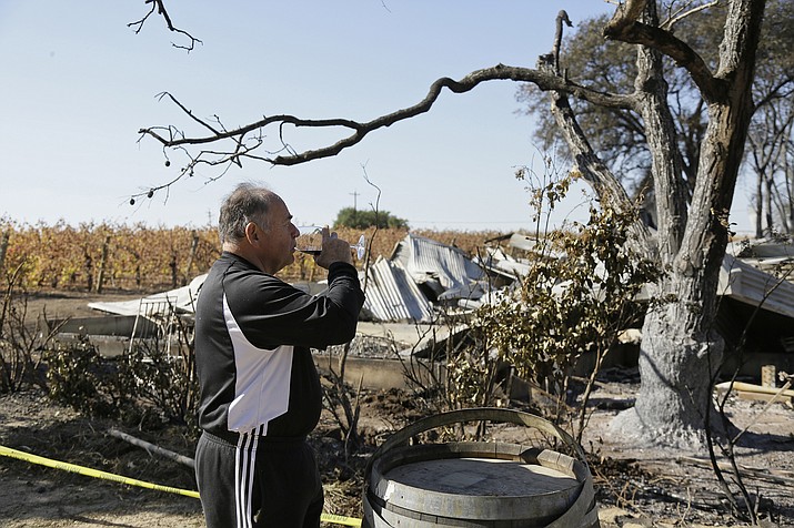Izzy Lewkosky of Kansas City, Kan., tastes a glass of Cabernet Sauvignon on Nov. 6, 2019, while looking out at the wildfire incinerated Soda Rock Winery in Healdsburg, Calif. (Eric Risberg/AP)