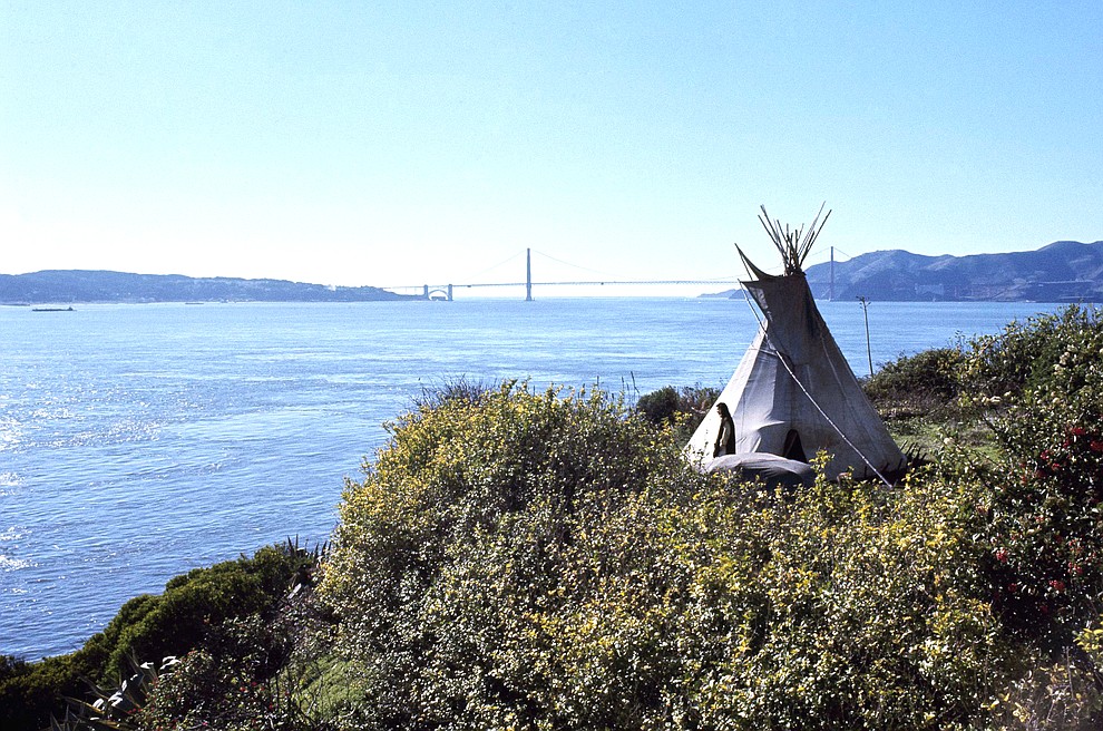 FILE - In this Nov. 18, 1970, file photo, Sioux Indian John Trudell stands next to the teepee he set up for himself during the Native American occupation of Alcatraz Island. The week of Nov. 18, 2019, marks 50 years since the beginning of a months-long Native American occupation at Alcatraz Island in the San Francisco Bay. The demonstration by dozens of tribal members had lasting effects for tribes, raising awareness of life on and off reservations, galvanizing activists and spurring a shift in federal policy toward self-determination. (AP Photo/File)