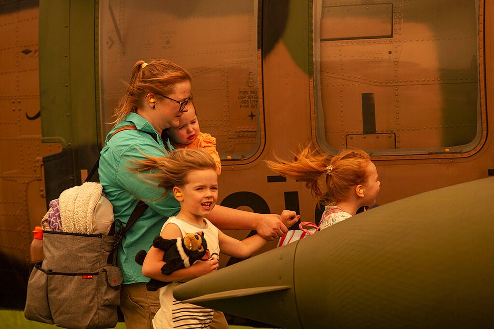 In this Jan. 4, 2020 photo provided by the Australian Department of Defence, a woman and three children prepare to board an Australian Army Blackhawk helicopter in Omeo, Victoria, Australia, for evacuation from the wildfire effected area. The wildfires have so far scorched an area twice the size of the U.S. state of Maryland. (Corporal Nicole Dorrett/ADF via AP)