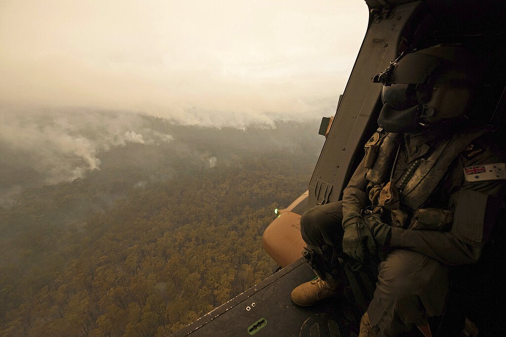 In this Sunday, Jan. 5, 2020, photo provided by Australian Department of Defence, a Royal Australian Navy MRH-90 helicopter crew member looks out over fires burning near Cann River, Australia. The wildfires have so far scorched an area twice the size of the U.S. state of Maryland. (Private Michael Currie/ADF via AP)