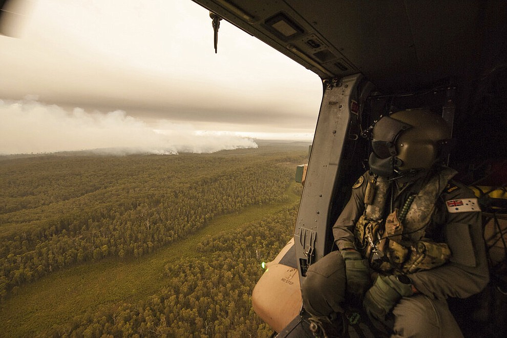 In this Sunday, Jan. 5, 2020, photo provided by Australian Department of Defence, a Royal Australian Navy MRH-90 helicopter crew member looks out over fires burning near Cann River. The wildfires have so far scorched an area twice the size of the U.S. state of Maryland. (Private Michael Currie/ADF via AP)