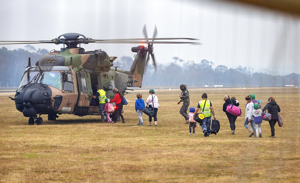 In this photo provided by the Australian Department of Defence, people walk to board a helicopter as the fire ravaged community of Mallacoota is evacuated, Sunday, Jan. 5, 2020. The wildfires have so far scorched an area twice the size of the U.S. state of Maryland. (Corporal Nicole Dorrett/ADF via AP)