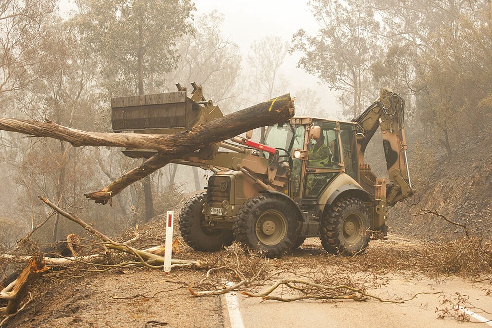 In this image released and dated on Jan. 6, 2020, from Australian Department of Defence, plant operators Cpl. Duncan Keith and Sapper Ian Larner of the 22nd Engineer Regiment use a 434 backhoe to assist staff from Forestry Management Victoria to clear fire damaged trees from the great Alpine road between Bairnsdale and Omeo during Operation Bushfire Assist 19-20 in Bairnsdale, Victoria, Australia. Australia's government on Monday said it was willing to pay “whatever it takes†to help communities recover from deadly wildfires that have ravaged the country. (Department of Defence via AP)