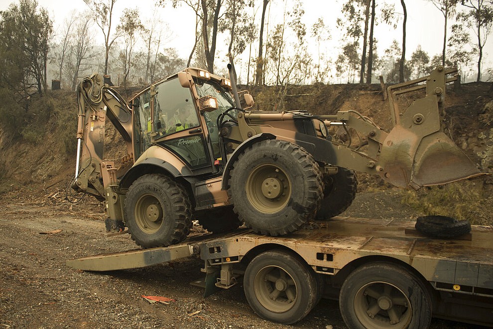 In the image released and dated Monday, Jan. 6, 2020, by the Australian Department of Defence, plant operators Cpl. Duncan Keith and Sapper Ian Larner of the 22nd Engineer Regiment use a 434 backhoe to assist staff from Forestry Management Victoria to clear fire damaged trees from the great Alpine road between Bairnsdale and Omeo during Operation Bushfire Assist 19-20 in Bairnsdale, Victoria, Australia. Australia's government on Monday said it was willing to pay “whatever it takes†to help communities recover from deadly wildfires that have ravaged the country. (Australia Department of Defence via AP)