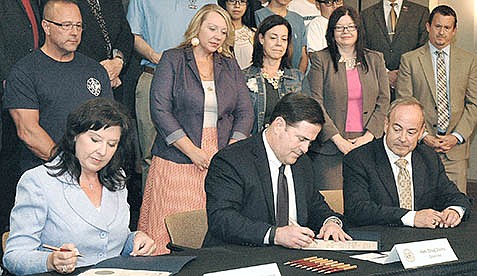 Gov. Doug Ducey, center, signs the certification of the results of the 2016 election to increase the amount taken from an education trust account for public schools. With him are then-Secretary of State Michele Reagan and Supreme Court Justice Clint Bolick. (Capitol Media Services photo by Howard Fischer)