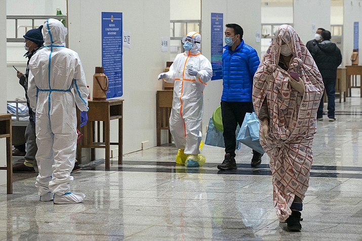 In this Wednesday, Feb. 5, 2020 photo, medical workers in a protective suit help patients who diagnosed with the coronaviruses as they arrive at a temporary hospital which transformed from an exhibition center in Wuhan in central China's Hubei province. Ten more people were sickened with a new virus aboard one of two quarantined cruise ships with some 5,400 passengers and crew aboard, health officials in Japan said Thursday, as China reported 73 more deaths and announced that the first group of patients were expected to start taking a new antiviral drug. (Chinatopix via AP)