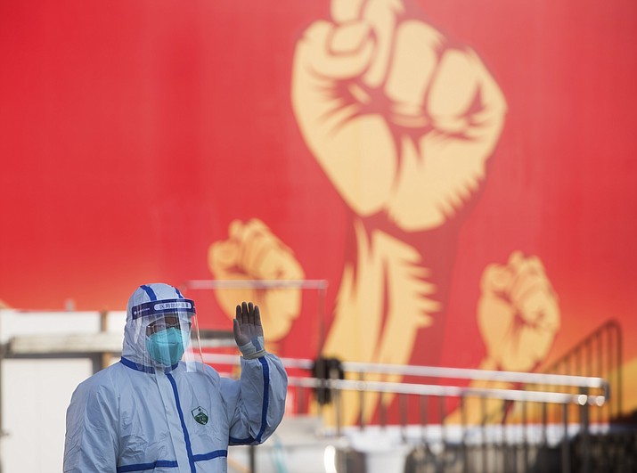 A medical worker waves near a propaganda poster as patients arrive at a temporary hospital with 1100 beds converted from the Wuhan Sports Center in Wuhan in central China's Hubei Province, Feb. 12, 2020. Without enough facilities to handle the number of cases of viral infection, Wuhan has been building prefabricated hospitals and converting a gym and other large spaces to house patients and try to isolate them from others. (Xiao Yijiu/Xinhua via AP)