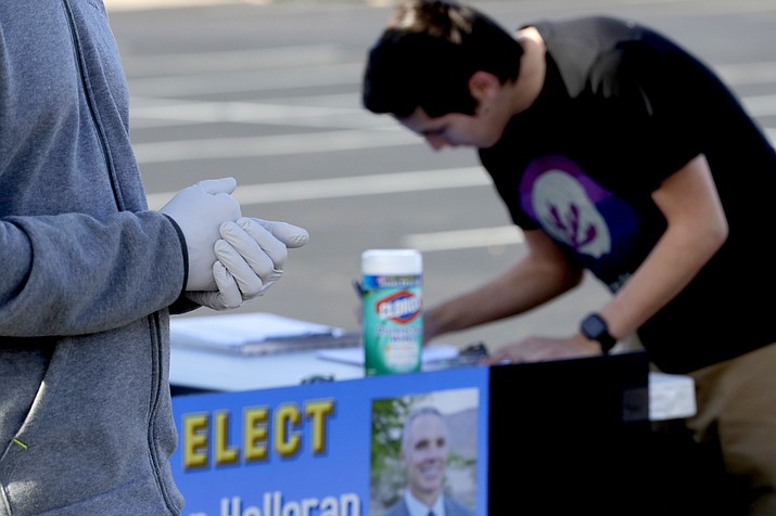 Constable candidate Ben Halloran wears latex gloves and provides disinfectant wipes to voters as they sign his petition to get on the November ballot outside of a polling station Tuesday, March 17, 2020, in Phoenix. (Matt York/AP)