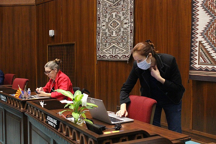 State Rep. Jennifer Jermaine, wearing a mask, looks at documents on her computer as fellow Democratic Rep. Jennifer Longdon, left, looks at her phone before the start of an unusual floor session at the Arizona House in Phoenix, on Thursday, March 19, 2020. The Legislature could work long into the night to enact a basic state budget and fixes for schools and workers before adjourning to allow the coronavirus crisis to ebb. (AP Photo/Bob Christie)