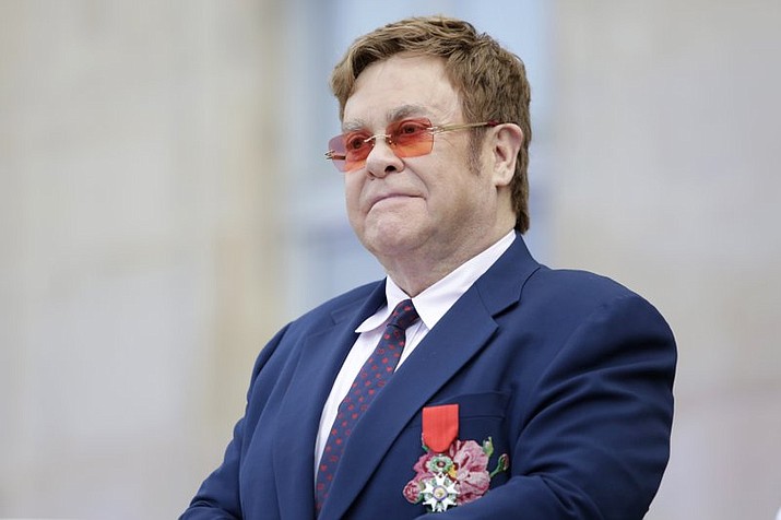 This June 21, 2019 file photo shows Elton John at a ceremony honoring him with the Legion of Honor in Paris. John is hosting a “living room” concert aimed at bolstering American spirits during the coronavirus crisis and saluting those countering it. The event was announced Wednesday by iHeartMedia and Fox. Alicia Keys, Billie Eilish, Mariah Carey, the Backstreet Boys, Tim McGraw and Billie Joe Armstrong are scheduled to take part in the concert airing at 9-10 p.m. Eastern Sunday on Fox TV and on iHeartMedia radio stations. (AP Photo/Lewis Joly, Pool)