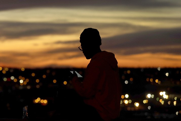 In this March 25, 2020, file photo, a person looks at a phone as the sun sets, in Kansas City, Mo. The city along with neighboring counties is under Stay at Home orders to help prevent the spread of COVID-19, the disease caused by the new coronavirus. (Charlie Riedel/AP file photo)