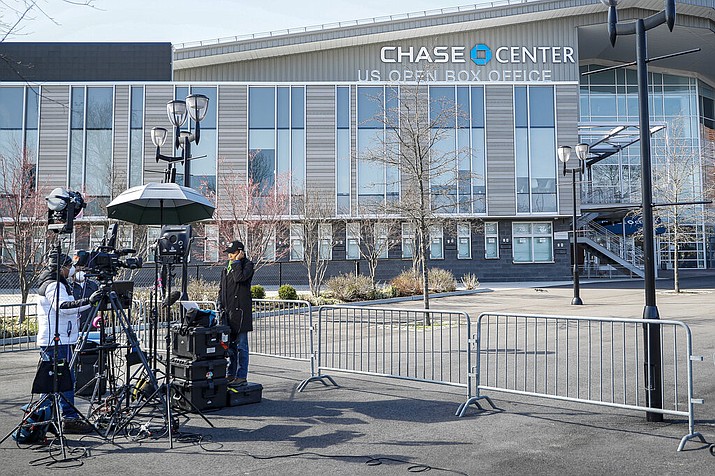In this April 1, 2020, photo, a news crew wearing personal protective equipment due to COVID-19 concerns reports outside the Chase Center that will become a makeshift hospital at the USTA Billie Jean King National Tennis Center in the Queens borough of New York. People desperate for information are more reliant than ever on local media as the coronavirus spreads across the U.S. But newspapers, magazines and digital publishers are feeling the pressure as advertising craters. (AP Photo/John Minchillo)