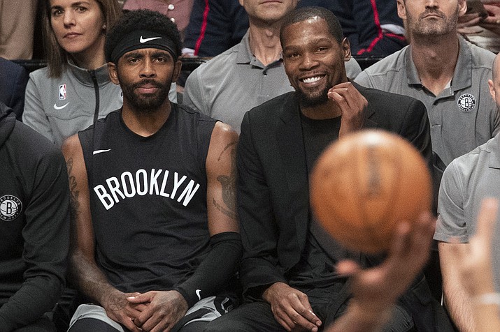 In this Nov. 1, 2019, file photo, Brooklyn Nets' Kyrie Irving, left, and Kevin Durant watch the game action from the bench during the second half of an NBA basketball game against the Houston Rockets in New York. With so much uncertainty around the NBA season, Brooklyn Nets general manager Sean Marks is no longer ruling Kevin Durant out for the season. Marks had repeatedly said he didn't expect Durant to play this season while recovering from Achilles tendon surgery, but he acknowledged Wednesday that everything is unknown now that the season is suspended because of the new coronavirus. Even Kyrie Irving, who had shoulder surgery on March 3, might be available if play stretched into the summer. (AP Photo/Mary Altaffer, File)
