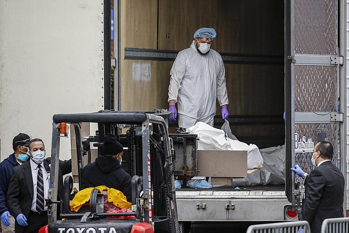A body wrapped in plastic is loaded onto a refrigerated container truck used as a temporary morgue by medical workers wearing personal protective equipment due to COVID-19 concerns, Tuesday, March 31, 2020, at Brooklyn Hospital Center in the Brooklyn borough of New York. The new coronavirus causes mild or moderate symptoms for most people, but for some, especially older adults and people with existing health problems, it can cause more severe illness or death. (John Minchillo/AP)