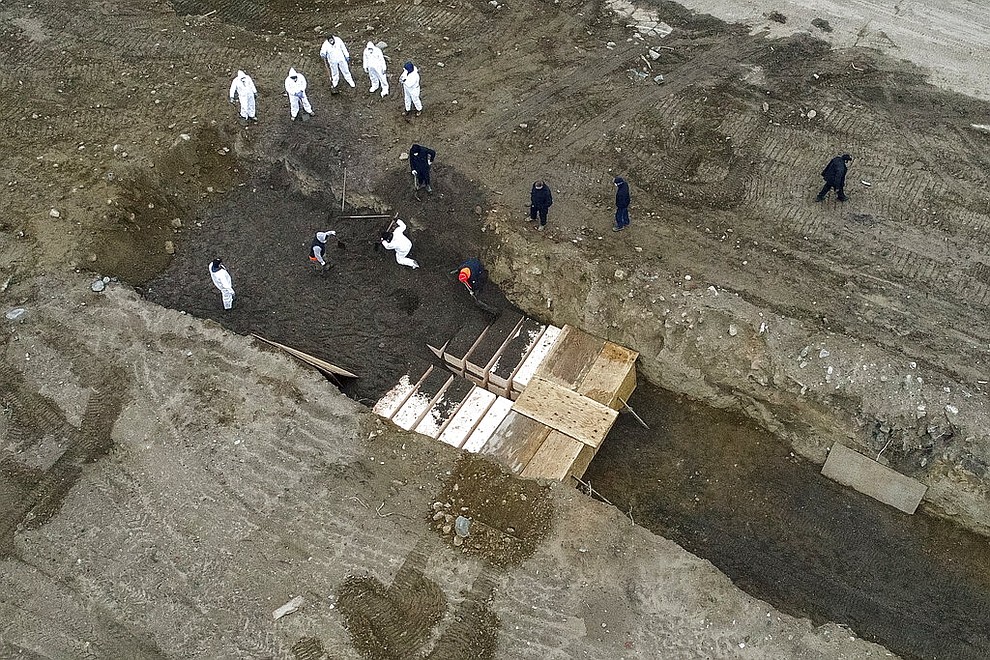 Workers wearing personal protective equipment bury bodies in a trench on Hart Island, Thursday, April 9, 2020, in the Bronx borough of New York. On Thursday, New York City’s medical examiner confirmed that the city has shortened the amount of time it will hold on to remains to 14 days from 30 days before they will be transferred for temporary internment at a City Cemetery. Earlier in the week, Mayor Bill DeBlasio said that officials have explored the possibility of temporary burials on Hart Island, a strip of land in Long Island Sound that has long served as the city’s potter’s field. (AP Photo/John Minchillo)