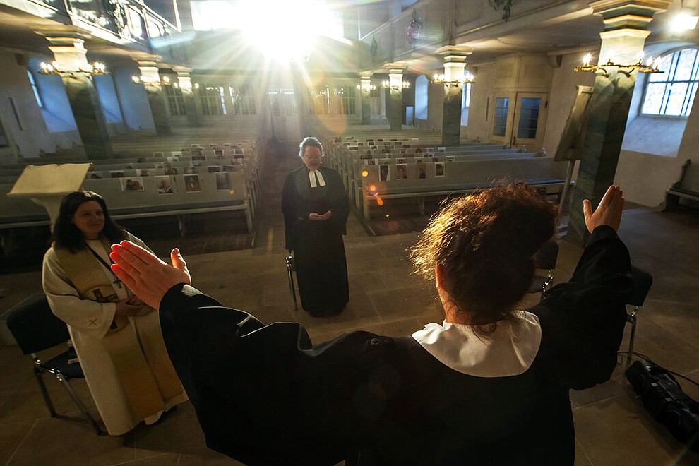 Vicar Kerstin Gommel, right, celebrates the Maundy Thursday Service besides Dean Jana Petri, left, and youth pastor Anna Boeck, center, in the empty Protestant church St. Marien in Suhl, Germany, Thursday, April 9, 2020. The church members are present symbolically with their portrait fixed to the pews. Due to the coronavirus no services are held these days. (AP Photo/Jens Meyer)