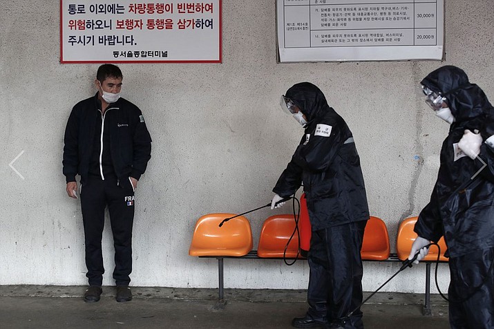 A passenger, left, stands as the members of reserved forces units wearing protective gears disinfect chairs as a precaution against the new coronavirus at a bus terminal in Seoul, South Korea, Thursday, March 12, 2020. South Korea announced plans Saturday to strap tracking wristbands on people who defy quarantine orders. (Lee Jin-man/Associated Press, file)