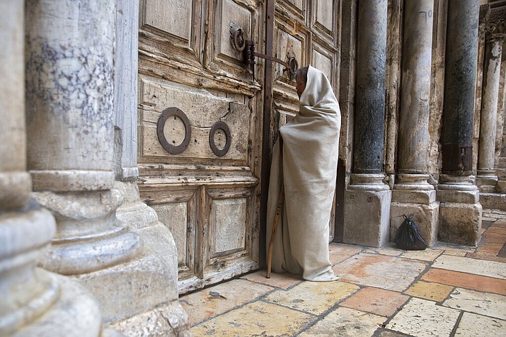 A Christian worshiper stands at the closed door of the Church of the Holy Sepulchre, believed by many Christians to be the site of the crucifixion and burial of Jesus Christ, in Jerusalem, Friday, April 10, 2020. Christians are commemorating Jesus' crucifixion without the solemn church services or emotional processions of past years, marking Good Friday in a world locked down by the coronavirus pandemic.(AP Photo/Sebastian Scheiner)