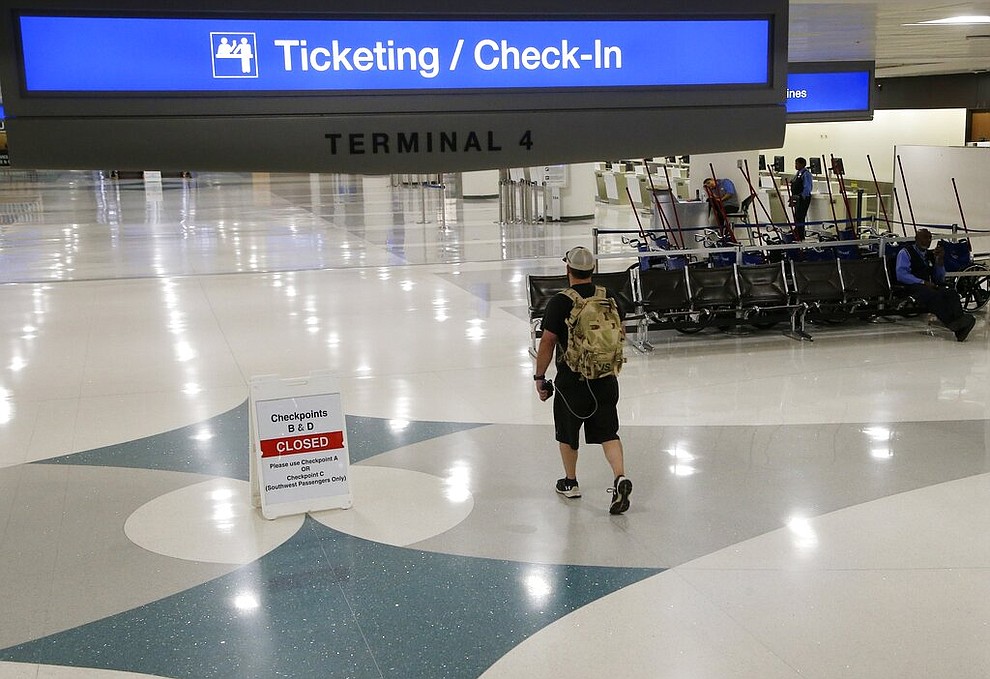 A lone passenger walks to check in at a desolate Phoenix Sky Harbor International Airport Tuesday, April 14, 2020, in Phoenix. The coronavirus has caused a significant decrease in air travel. (AP Photo/Ross D. Franklin)