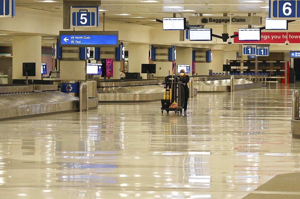 A member of the cleaning crew pushes a cart through an empty baggage claim area at Phoenix Sky Harbor International Airport on Tuesday, April 14, 2020, in Phoenix. The coronavirus outbreak has caused a significant decrease in air travel. (AP Photo/Ross D. Franklin)