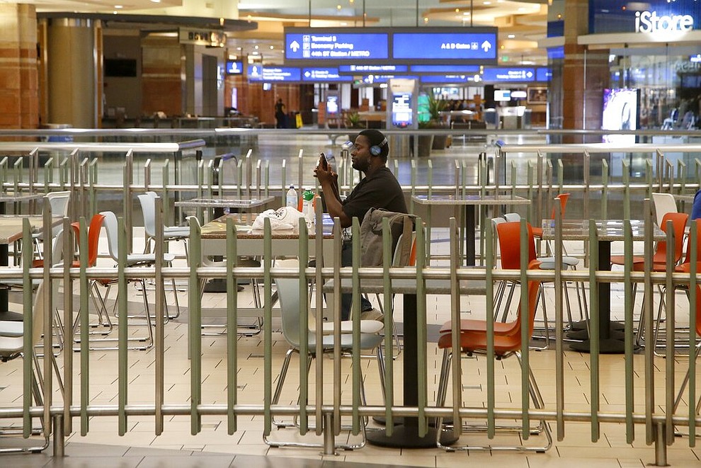 A lone passenger sits in an otherwise empty food court at Phoenix Sky Harbor International Airport on Tuesday, April 14, 2020, in Phoenix. The coronavirus outbreak has caused a significant decrease in air travel. (AP Photo/Ross D. Franklin)