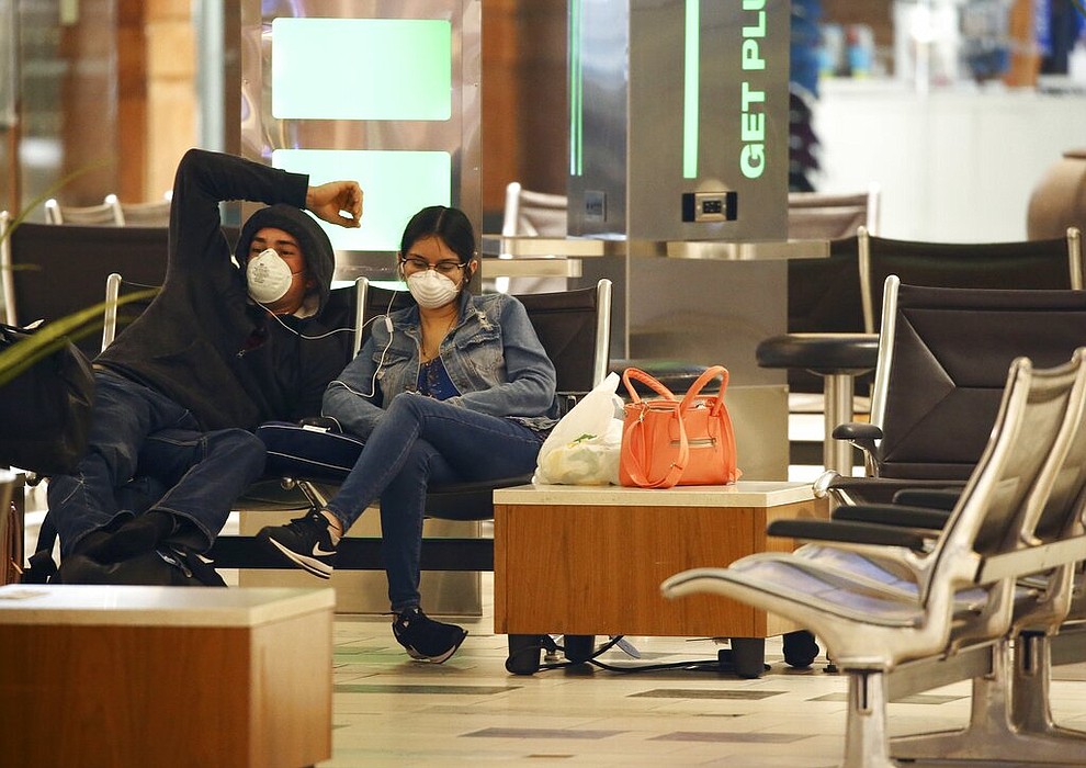 Two passengers wearing face coverings wait for a flight at Phoenix Sky Harbor International Airport on Tuesday, April 14, 2020, in Phoenix. The coronavirus outbreak has caused a significant decrease in air travel. (AP Photo/Ross D. Franklin)