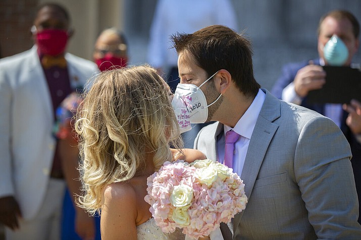 Gabrielle Schmees, 29, and Diego Grassano, 31, kiss wearing protective masks on the day of their wedding at the Gerald D. Hines Waterwall Park on Monday, April 27, 2020, in Houston. Because of COVID-19, the couple decided to postpone their official wedding and have a small one at the Waterwall Park until December when they can have the official one with all of their family and friends. (Marie De Jesus/Houston Chronicle via AP)