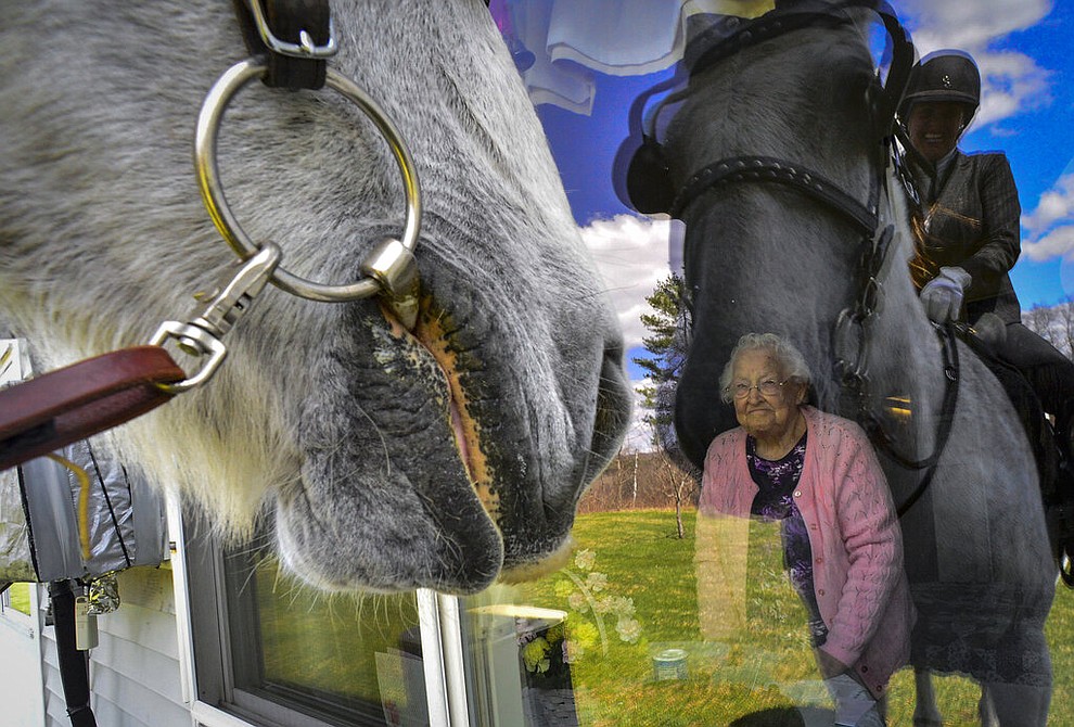 A resident of Vernon Green Nursing Home, in Vernon, Vt., looks out her window as Lisa Tyler, owner of Forever Dream Drafts, visits the nursing home with her horse to try to bring a smile to the faces of the residents and staff members April 15, 2020. The nursing home is sheltering-in-place because of the COVID-19 pandemic to help prevent the residents from contracting the virus. (Kristopher Radder/The Brattleboro Reformer via AP)