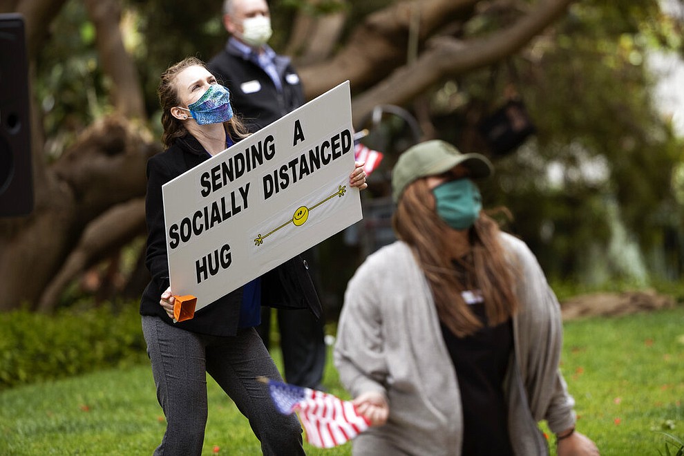 Employees of Vi at La Jolla retirement complex hold signs and wave flags for the residents during an afternoon pep rally, April 8, 2020, in San Diego. As elderly residents who have been quarantined for weeks make their way out onto their balconies, employees below dance, wave flags and shout words of encouragement in a now almost daily afternoon pep rally. (AP Photo/Gregory Bull)