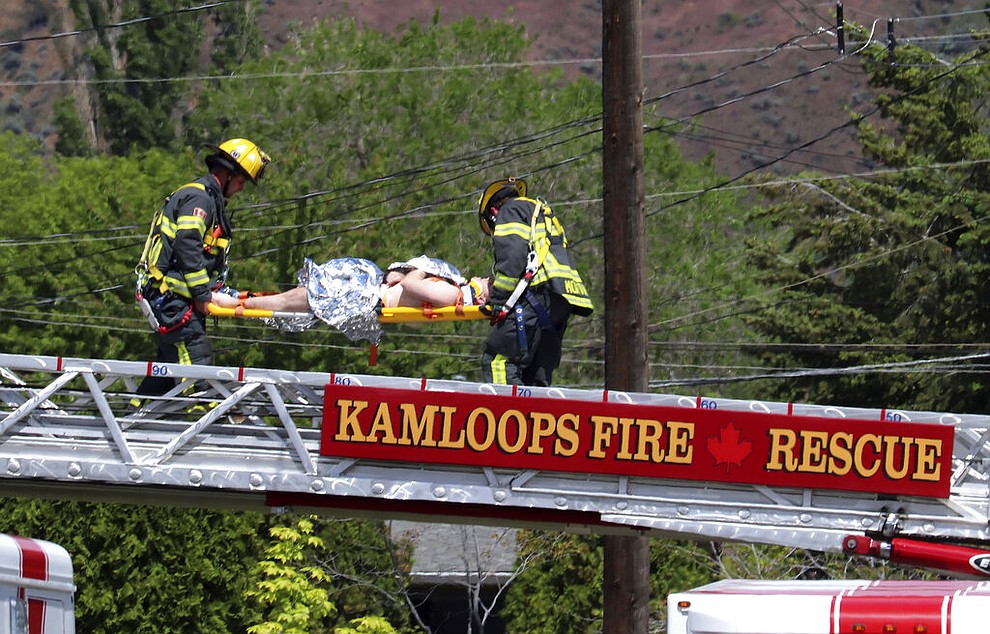 First responders carry an injured person on a stretcher across a fire truck ladder from a rooftop at the scene of a crash involving a Canadian Forces Snowbirds aircraft in Kamloops, British Columbia, Sunday, May 17, 2020. (Brendan Kergin/Castanet Kamloops/The Canadian Press via AP)
