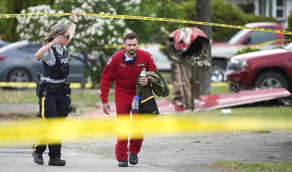 The remains of a downed Canadian Forces Snowbird plane is pictured as a member of the Snowbirds walks past in Kamloops, Canada, Sunday, May 17, 2020. The Canadian acrobatic jet crashed into the British Columbia neighborhood Sunday during a flyover intended to boost morale during the pandemic, killing at least one crew member, seriously injuring another and setting a house on fire. (Jonathan Hayward/The Canadian Press via AP)