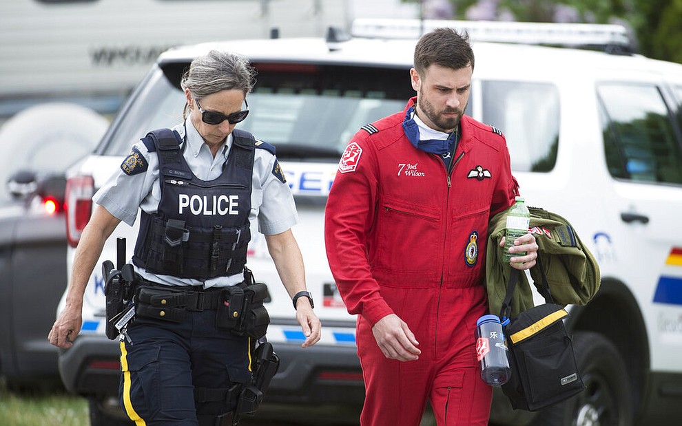 Canadian Forces Snowbird pilot Joel Wilson, with a police officer, walks past the crash site of one of his team's airplanes in Kamloops, Canada, Sunday, May 17, 2020. The Canadian acrobatic jet crashed into the British Columbia neighborhood Sunday during a flyover intended to boost morale during the pandemic, killing at least one crew member, seriously injuring another and setting a house on fire. (Jonathan Hayward/The Canadian Press via AP)