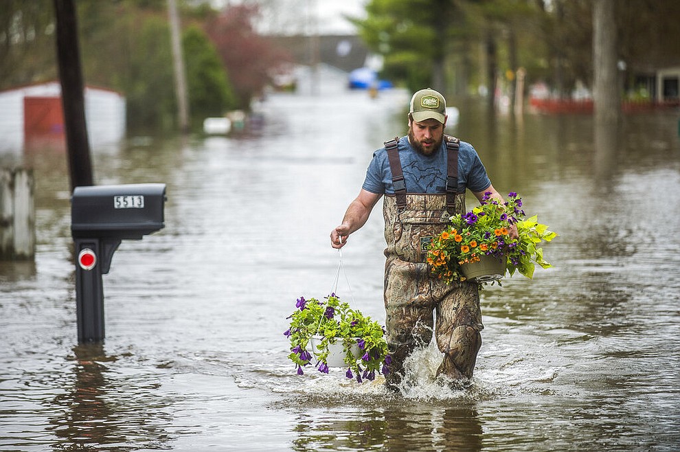 Tyler Marciniak of Grand Rapids carries hanging plants through floodwater as he helps his father, Tom Marciniak, assess the damage to his home on Red Oak Drive on Wixom Lake, Tuesday, May 19, 2020 in Beaverton, Mich. (Katy Kildee/Midland Daily News via AP)
