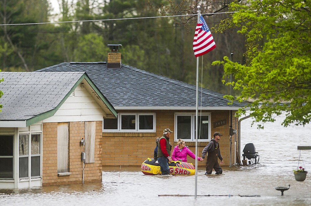 People help each other travel from one home to another using an inflatable raft on Oakridge Road on Wixom Lake, Tuesday, May 19, 2020 in Beaverton, Mich. People living along two mid-Michigan lakes and parts of a river have been evacuated following several days of heavy rain that produced flooding and put pressure on dams in the area. (Katy Kildee/Midland Daily News via AP)