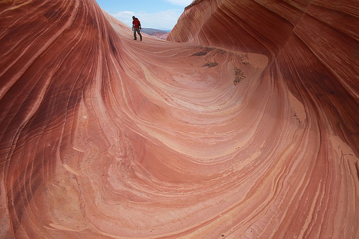 In this May 28, 2013, file photo, a hiker walks on a rock formation known as The Wave in the Vermilion Cliffs National Monument in Arizona. A walk-in lottery for the popular Arizona hike could move online. Half of the 20 permits for one of the most exclusive and dramatic hiking spots in the southwestern United States remain unavailable during the coronavirus pandemic. The virus hasn't forced the closure of the Wave in the Vermillion Cliffs National Monument along the Arizona-Utah border. But it has suspended a daily, in-person lottery for 10 permits because the agency that oversees it can't ensure social distancing. (AP Photo/Brian Witte, File)
