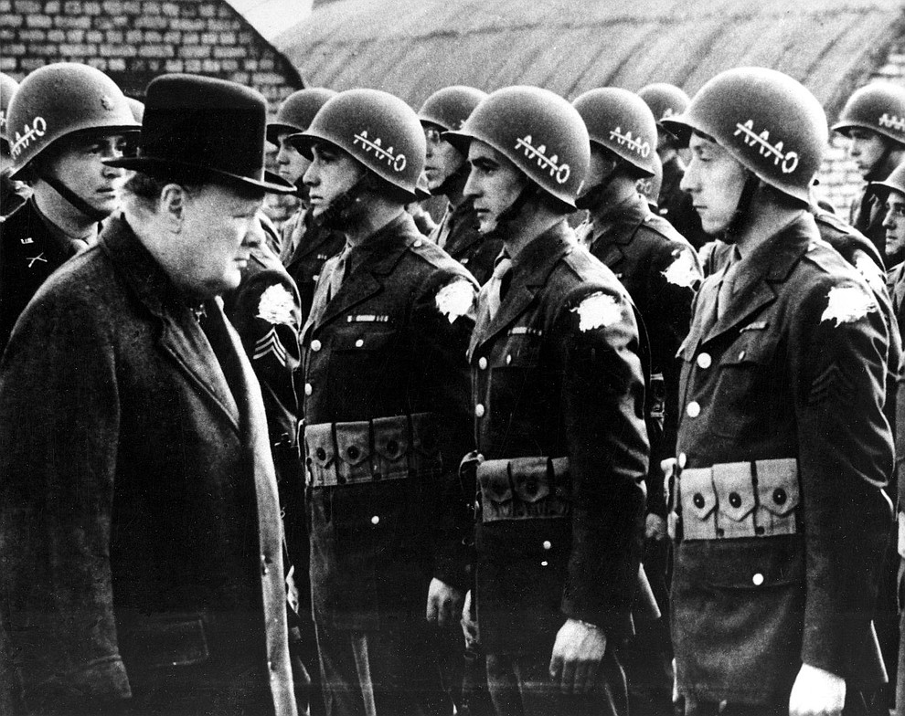 British Prime Minister Winston Churchill, left, reviews American troops at a base in England on the eve of D-Day, June 1944, during World War II. The initials AAAO on the steel helmets with a line across the As stands for "Anywhere, Anytime, Anyhow, Bar Nothing." The identification shoulder patches of the G.I.s are blotted out by the censor. (AP Photo)..