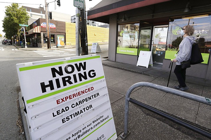 In this photo taken Thursday, June 4, 2020, a pedestrian wearing a mask walks past reader board advertising a job opening for a remodeling company, in Seattle. The U.S. unemployment rate fell to 13.3% in May, and 2.5 million jobs were added — a surprisingly positive reading in the midst of a recession that has paralyzed the economy and depressed the job market in the wake of the viral pandemic. (AP Photo/Elaine Thompson)