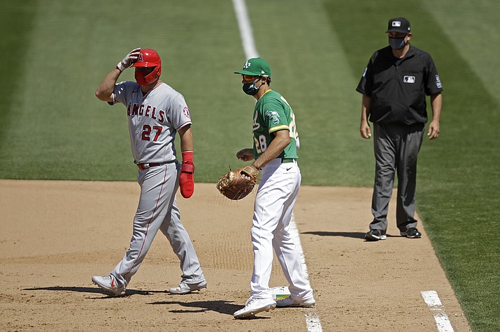 In this Monday, July 27, 2020, file photo, Oakland Athletics' Matt Olson (28) wears a mask as Los Angeles Angels' Mike Trout, left, also wears one while taking a lead off first base during the eighth inning of a baseball game in Oakland, Calif. Baseball's Western Divisions have so far avoided any COVID-related schedule disruptions and they're trying to keep it that way. (Ben Margot, AP File)