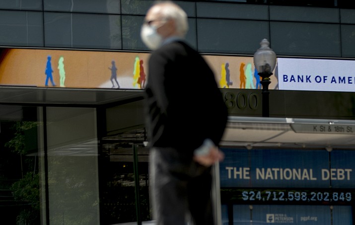 In this April 29, 2020 photo, a man waits to cross the street as a digital sign displays groups of people walking above another sign displaying the size of the national debt along an empty K Street in Washington. The U.S. budget deficit hit an all-time high of $3 trillion for the first 11 months of this budget year, the Treasury Department said Friday, Sept. 11, 2020. (Andrew Harnik/AP, File)