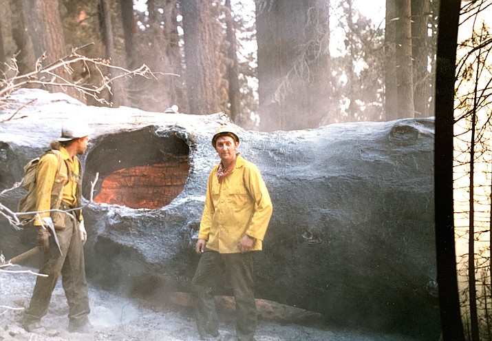 Wildland firefighter Kim Brown (right) poses for a picture next to a smoldering tree during a wildland fire assignment in the 1980s. (Photo courtesy of Kim Brown)