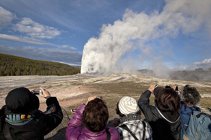 In this 2011, file photo, tourists photograph Old Faithful erupting on schedule late in the afternoon in Yellowstone National Park, Wyoming. Two West Valley City, Utah, men were ordered to serve two days in jail and pay $540 in fines and fees for cooking chickens in the hot spring, a Yellowstone spokeswoman said. (AP Photo/Julie Jacobson, File)