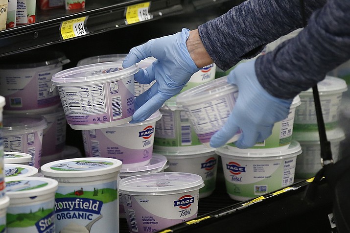 In this March 24, 2020 file photo, a woman reaches for yogurt wearing gloves during senior shopping hours at Homeland in Oklahoma City. To avoid any traces of the coronavirus that might be lurking on surfaces, Americans have been wiping down groceries, wearing surgical gloves in public and leaving mail packages out for an extra day or two. But experts say fear of being infected by touching something can be overblown. (Sue Ogrocki, AP File)