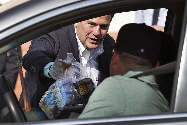 In this March 19, 2020 photo, Gov. Doug Ducey, left, hands a bag of food to a student outside Sunset Elementary School in Phoenix. Citing the state’s surge of COVID-19 cases, Arizona’s top education official on Saturday, Jan. 2, 2021, called for Ducey to order that public schools use only distance learning for the next two weeks without waivers from health officials. (Matt York/AP, file)
