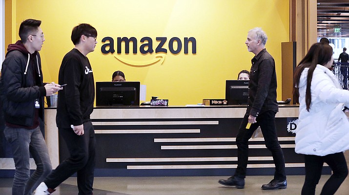 FILE - In this Nov. 13, 2018, file photo, employees walk through a lobby at Amazon's headquarters in Seattle. Amazon has announced $2 billion in loans and grants to secure affordable housing in three U.S. cities, including a Seattle suburb where the online retail giant employs at least 5,000 workers. Amazon said it would give $185.5 million to the King County Housing Authority to help buy affordable apartments in the region and keep the rents low, The Seattle Times reported Wednesday, Jan. 6, 2021. (Elaine Thompson/AP)
