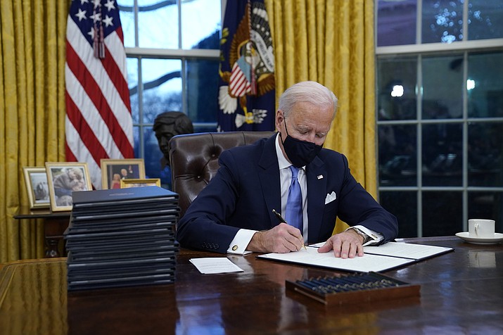 President Joe Biden signs his first executive order in the Oval Office of the White House on Wednesday, Jan. 20, 2021, in Washington. (Evan Vucci/AP)