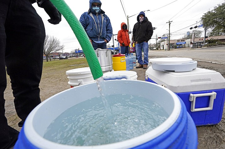 A water bucket is filled as others wait in near freezing temperatures to use a hose from public park spigot Thursday, Feb. 18, 2021, in Houston. Houston and several surrounding cities are under a boil water notice as many residents are still without running water in their homes. (AP Photo/David J. Phillip)