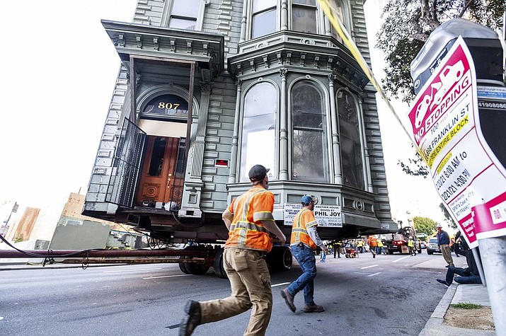 Workers pass a Victorian home as a truck pulls it through San Francisco on Sunday, Feb. 21, 2021. The house, built in 1882, was moved to a new location about six blocks away to make room for a condominium development. According to the consultant overseeing the project, the move cost approximately $400,000 and involved removing street lights, parking meters, and utility lines. (AP Photo/Noah Berger)