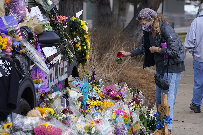 A mourner places a rose amid bouquets in tribute around a police cruiser for Boulder, Colo., police officer Eric Talley, who was one of 10 victims in Monday's mass shooting at a King Soopers grocery store, Wednesday, March 24, 2021, in Boulder, Colo. (David Zalubowski/AP)